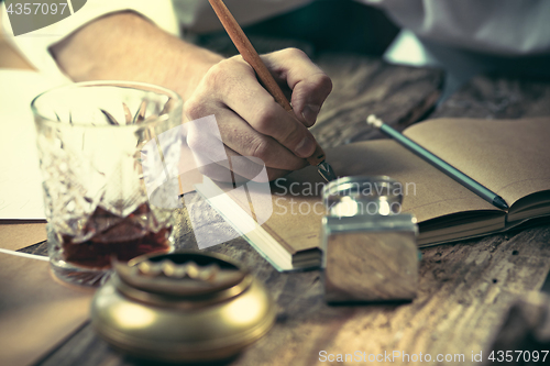 Image of Writer at work. The hands of young writer sitting at the table and writing something in his sketchpad