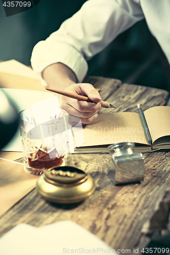 Image of Writer at work. Handsome young writer sitting at the table and writing something in his sketchpad