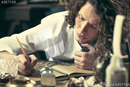 Image of Writer at work. Handsome young writer sitting at the table and writing something in his sketchpad