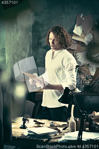 Image of Writer at work. Handsome young writer standing near the table and making up something in his mind