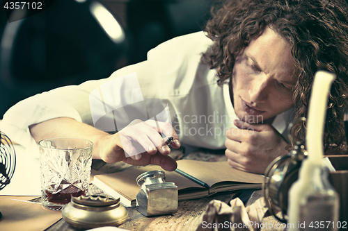 Image of Writer at work. Handsome young writer sitting at the table and writing something in his sketchpad