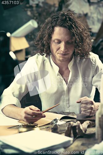 Image of Writer at work. Handsome young writer sitting at the table and writing something in his sketchpad