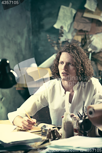 Image of Writer at work. Handsome young writer sitting at the table and writing something in his sketchpad