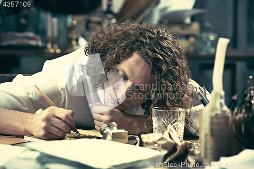 Image of Writer at work. Handsome young writer sitting at the table and writing something in his sketchpad