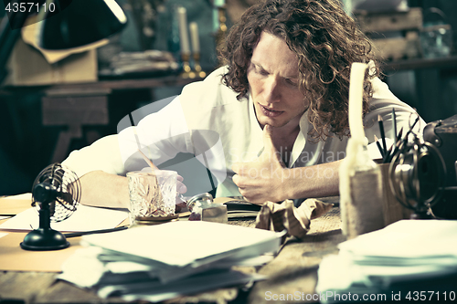 Image of Writer at work. Handsome young writer sitting at the table and writing something in his sketchpad