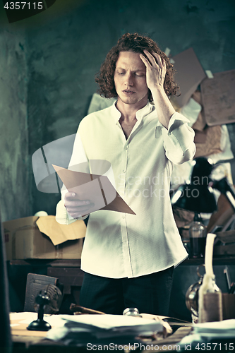 Image of Writer at work. Handsome young writer standing near the table and making up something in his mind