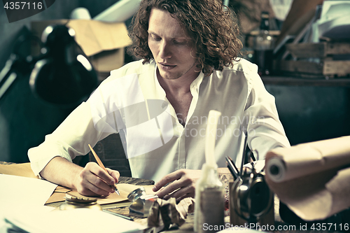 Image of Writer at work. Handsome young writer sitting at the table and writing something in his sketchpad