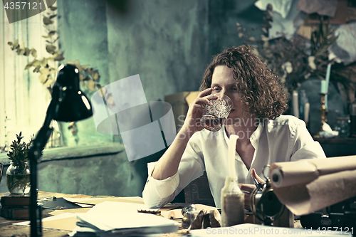 Image of Writer at work. Handsome young writer sitting at the table and writing something in his sketchpad