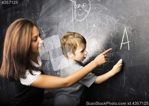 Image of little cute boy in glasses with young real teacher, classroom studying at blackboard school