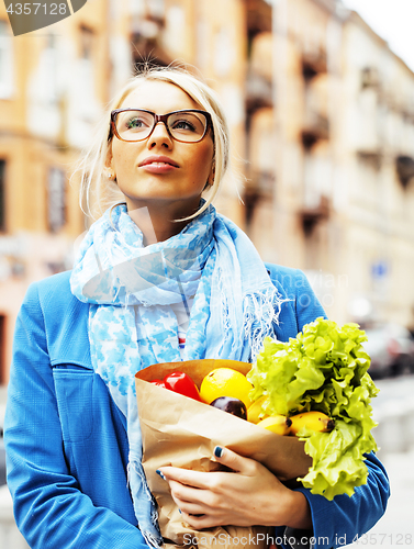 Image of young pretty blond woman with food in bag walking on street