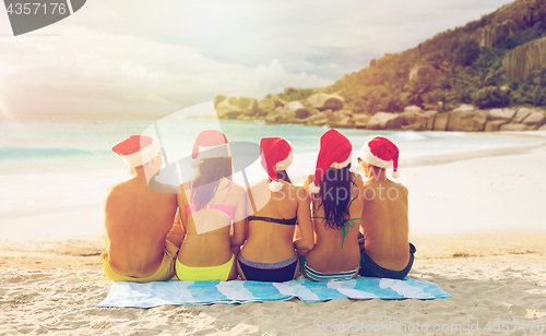 Image of friends in santa hats on beach at christmas