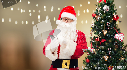 Image of santa claus with smartphone at christmas tree