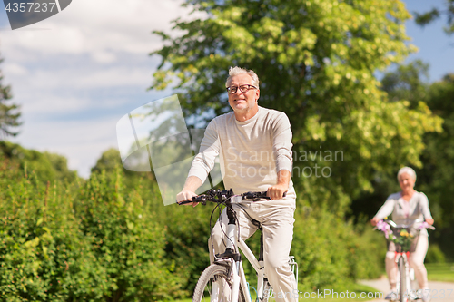 Image of happy senior couple riding bicycles at summer park