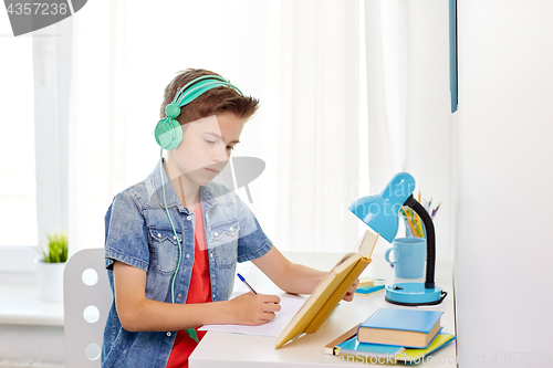 Image of student boy in headphones writing to notebook