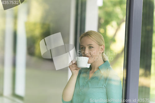 Image of young woman drinking morning coffee by the window