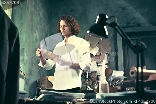 Image of Writer at work. Handsome young writer standing near the table and making up something in his mind