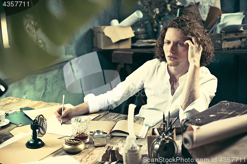 Image of Writer at work. Handsome young writer sitting at the table and writing something in his sketchpad