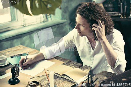 Image of Writer at work. Handsome young writer sitting at the table and writing something in his sketchpad