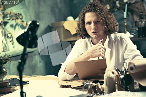 Image of Writer at work. Handsome young writer sitting at the table and writing something in his sketchpad