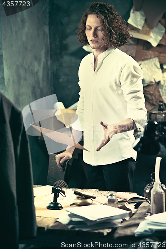 Image of Writer at work. Handsome young writer standing near the table and making up something in his mind