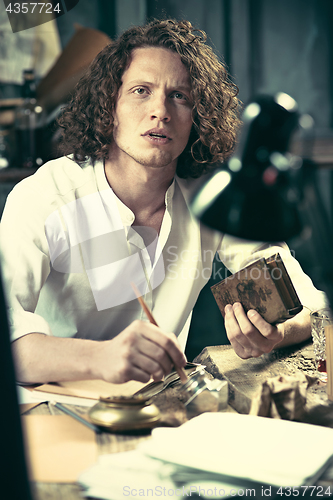 Image of Writer at work. Handsome young writer sitting at the table and writing something in his sketchpad