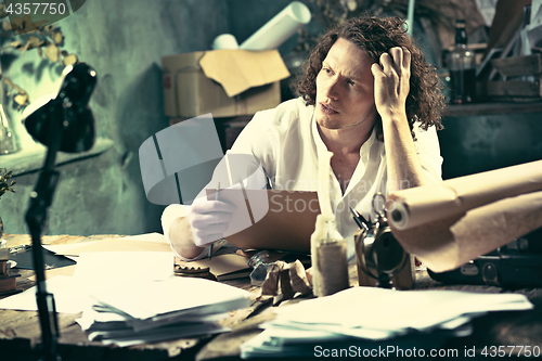 Image of Writer at work. Handsome young writer sitting at the table and writing something in his sketchpad