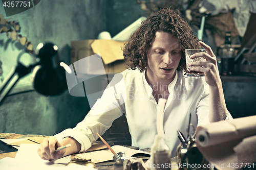 Image of Writer at work. Handsome young writer sitting at the table and writing something in his sketchpad