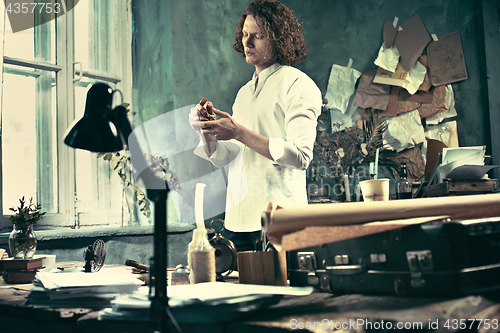 Image of Writer at work. Handsome young writer standing near the table and making up something in his mind