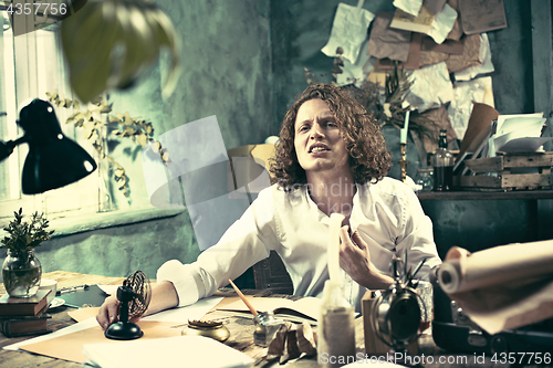 Image of Writer at work. Handsome young writer sitting at the table and writing something in his sketchpad