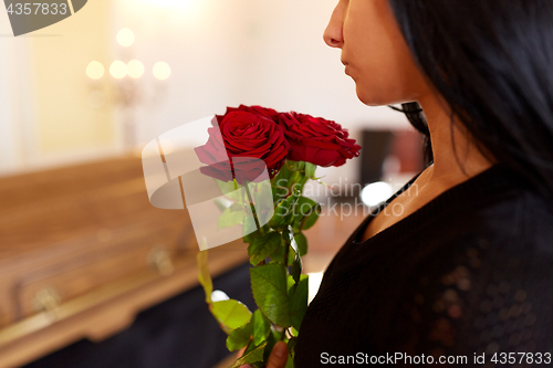 Image of woman with red roses and coffin at funeral