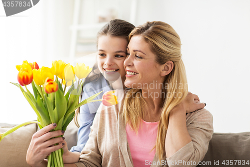 Image of happy girl giving flowers to mother at home