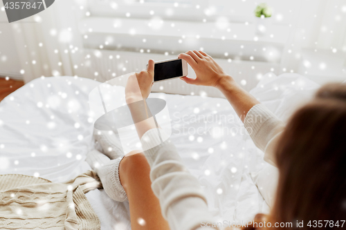 Image of woman photographing with smartphone in bet at home