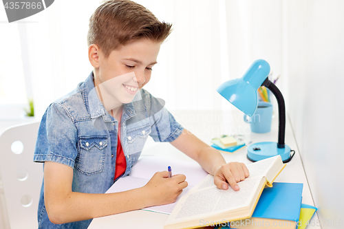 Image of student boy with book writing to notebook at home