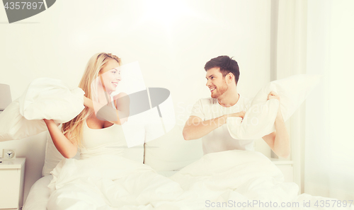 Image of happy couple having pillow fight in bed at home