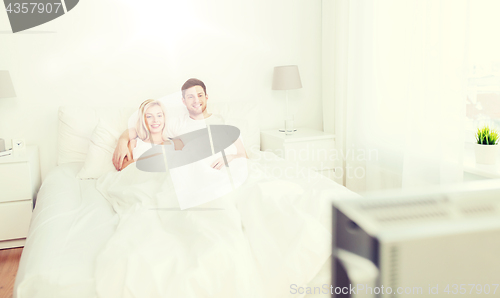 Image of happy couple lying in bed at home and watching tv