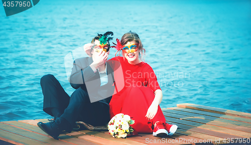 Image of Happy Couple In Masquerade Masks Against A Turquoise Lake