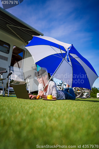 Image of Woman on the grass, looking at the laptop under umbrella near th