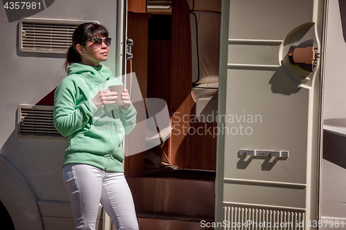 Image of Woman is standing with a mug of coffee near the camper RV.