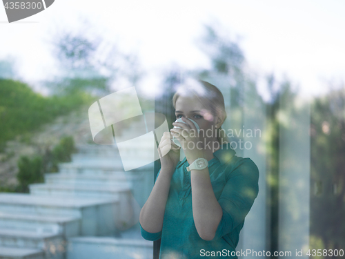 Image of young woman drinking morning coffee by the window