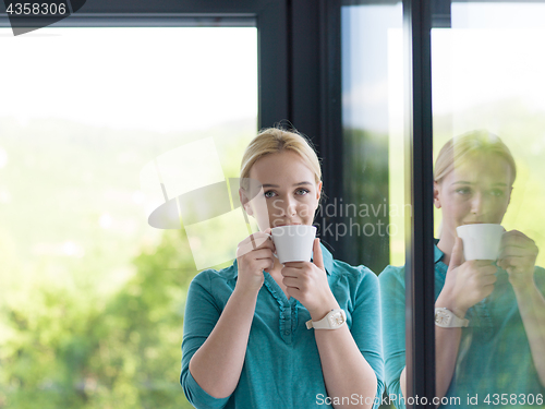 Image of young woman drinking morning coffee by the window