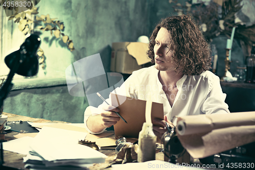 Image of Writer at work. Handsome young writer sitting at the table and writing something in his sketchpad