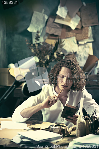 Image of Writer at work. Handsome young writer sitting at the table and writing something in his sketchpad