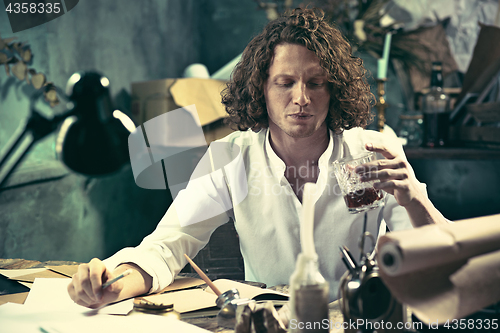 Image of Writer at work. Handsome young writer sitting at the table and writing something in his sketchpad