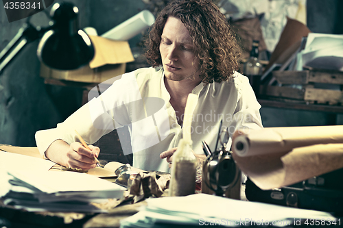 Image of Writer at work. Handsome young writer sitting at the table and writing something in his sketchpad