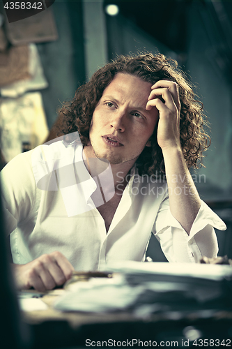 Image of Writer at work. Handsome young writer sitting at the table and writing something in his sketchpad