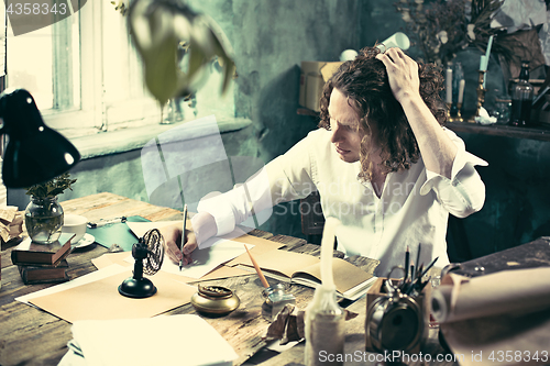 Image of Writer at work. Handsome young writer sitting at the table and writing something in his sketchpad