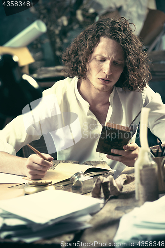 Image of Writer at work. Handsome young writer sitting at the table and writing something in his sketchpad