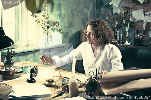 Image of Writer at work. Handsome young writer sitting at the table and writing something in his sketchpad