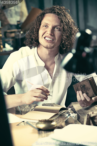 Image of Writer at work. Handsome young writer sitting at the table and writing something in his sketchpad