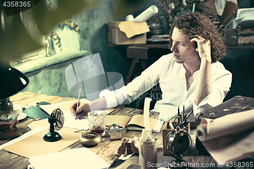 Image of Writer at work. Handsome young writer sitting at the table and writing something in his sketchpad